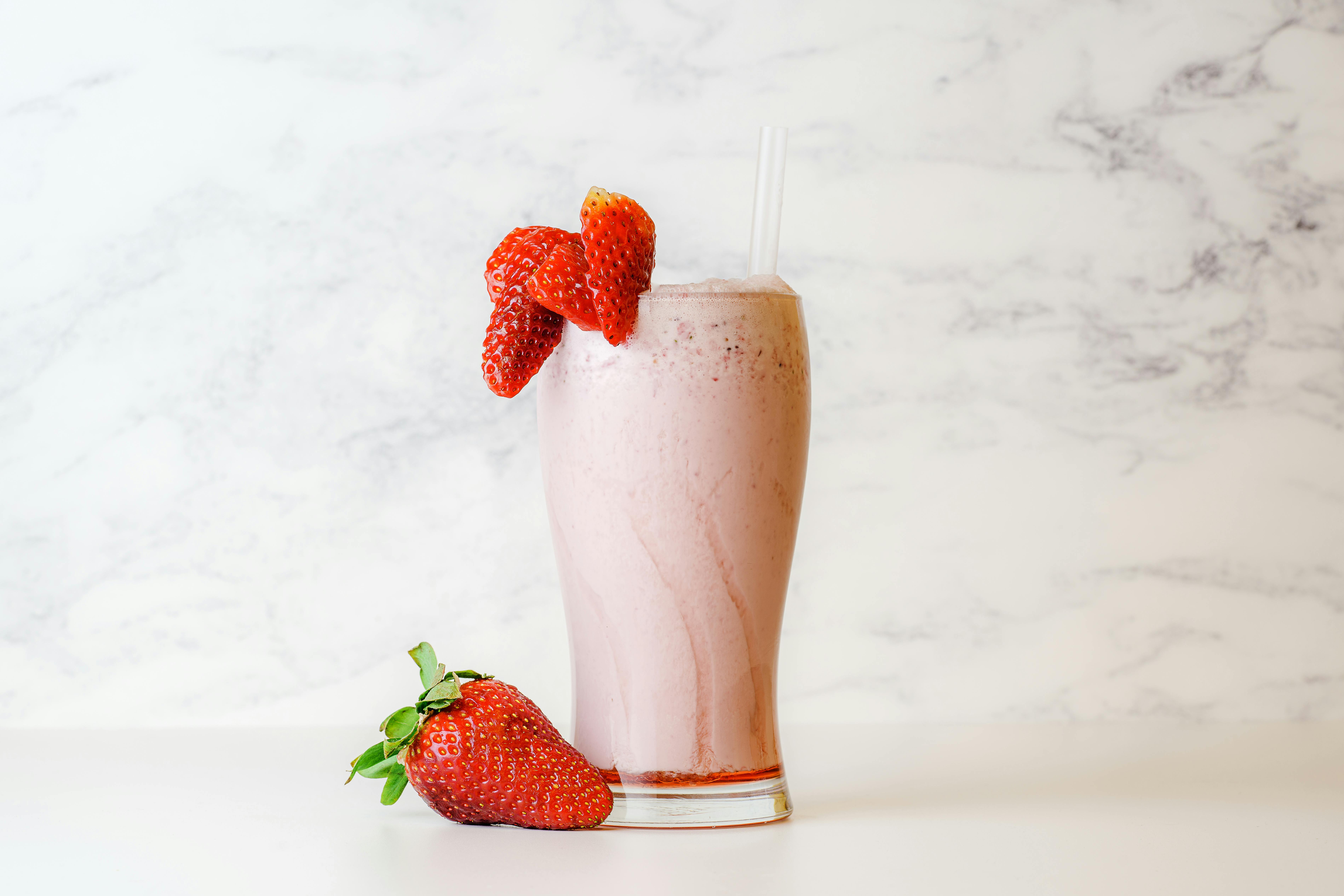 Delicious and creamy strawberry milkshake garnished with fresh berries on a white marble background.